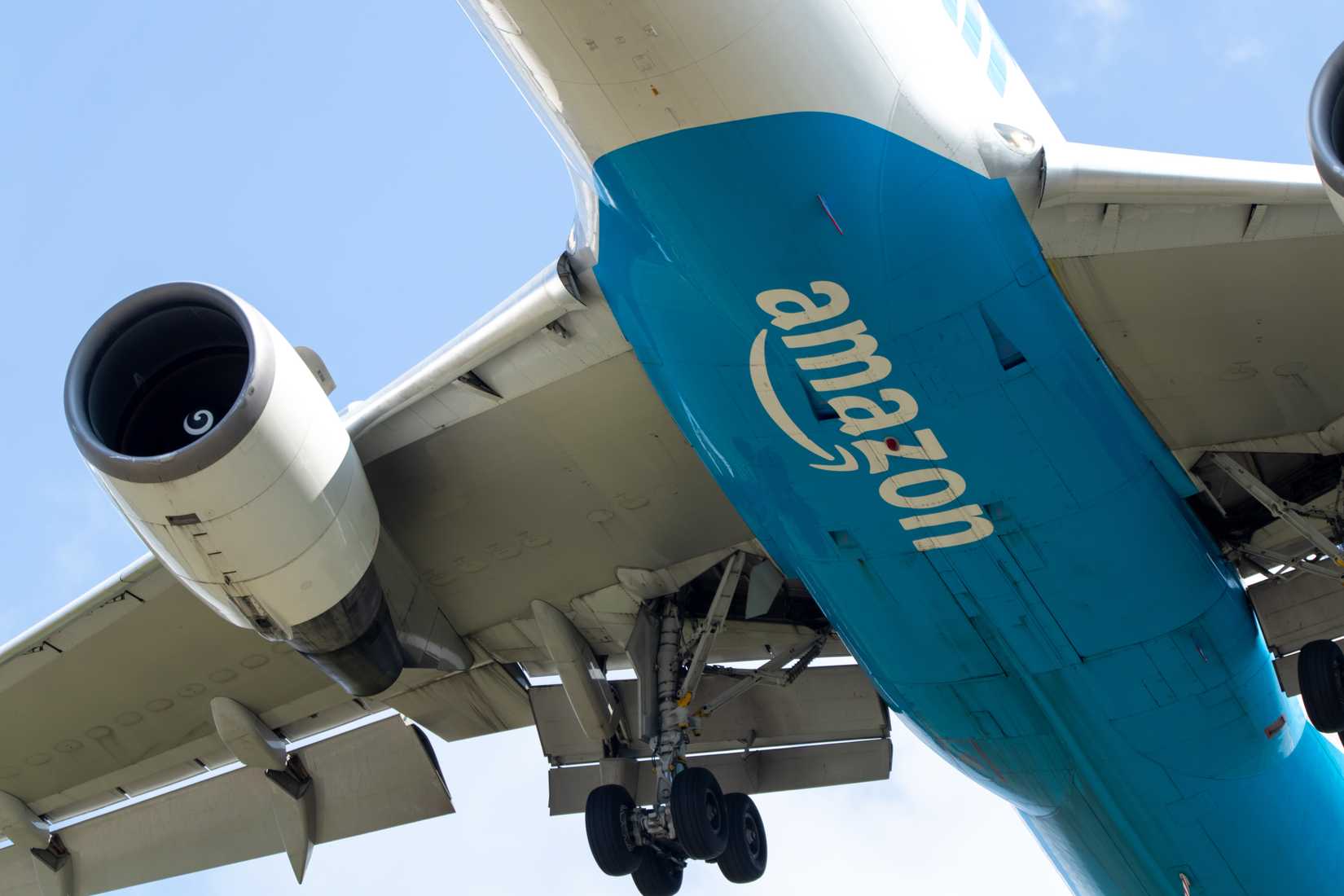 The Amazon logo on the bottom of a Prime Air Boeing 767 while landing on a clear and sunny day.