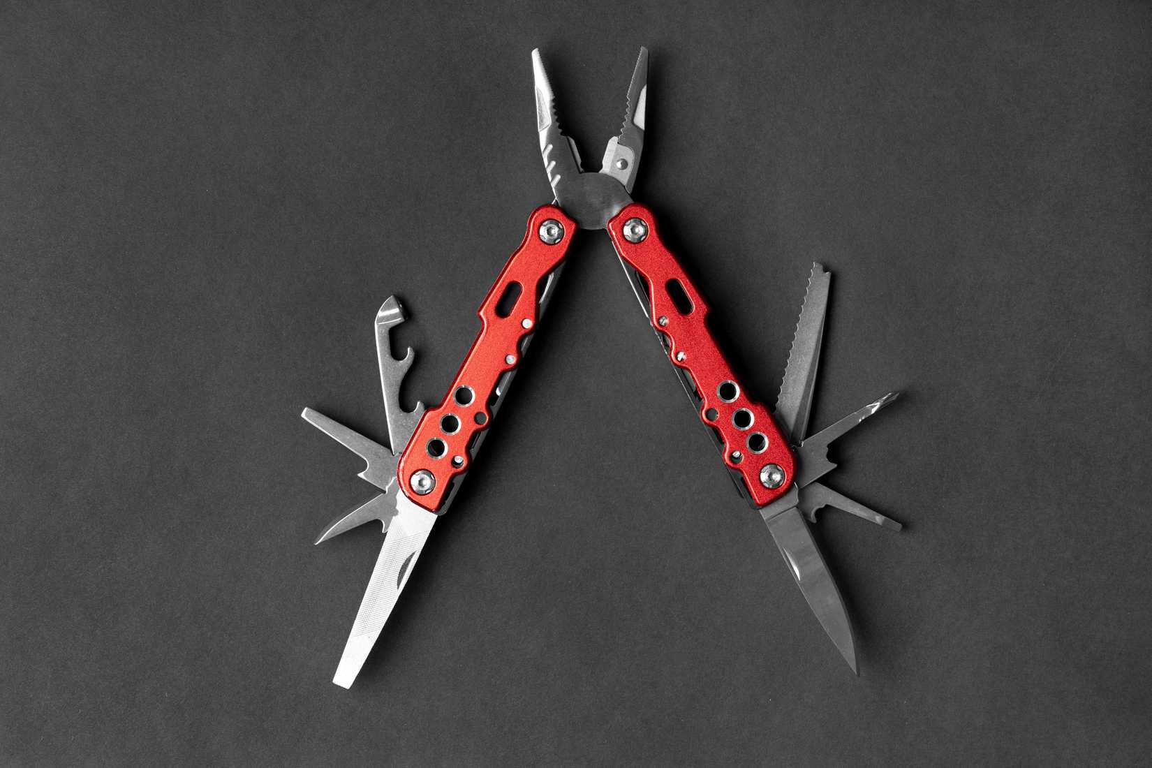 universal multifunctional knife pliers with different nozzles and a red handle on a dark gray background. Versatile camping knife. Multifunctional tool.