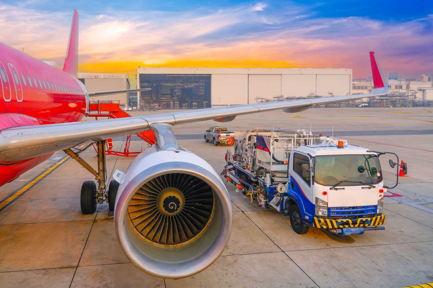 Airplane being preparing ready for takeoff in international airport. The fuel truck has arrived and is standing nearby wing, against the backdrop of aerospace hangar.