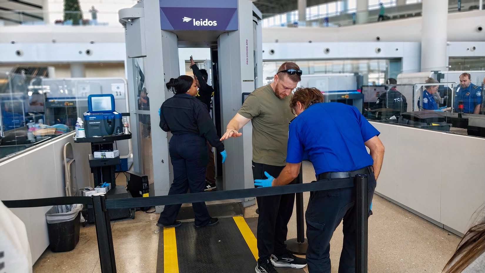 A TSA screener stands while patting down a passenger at a security checkpoint