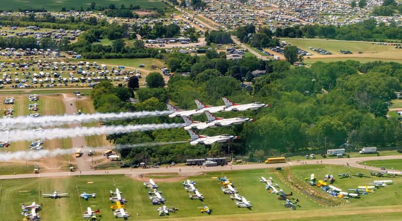 A photo of the US Air Force Thunderbirds flying over the EAA airshow. An airfield parking area is seen below with the campground in the backgroud. 