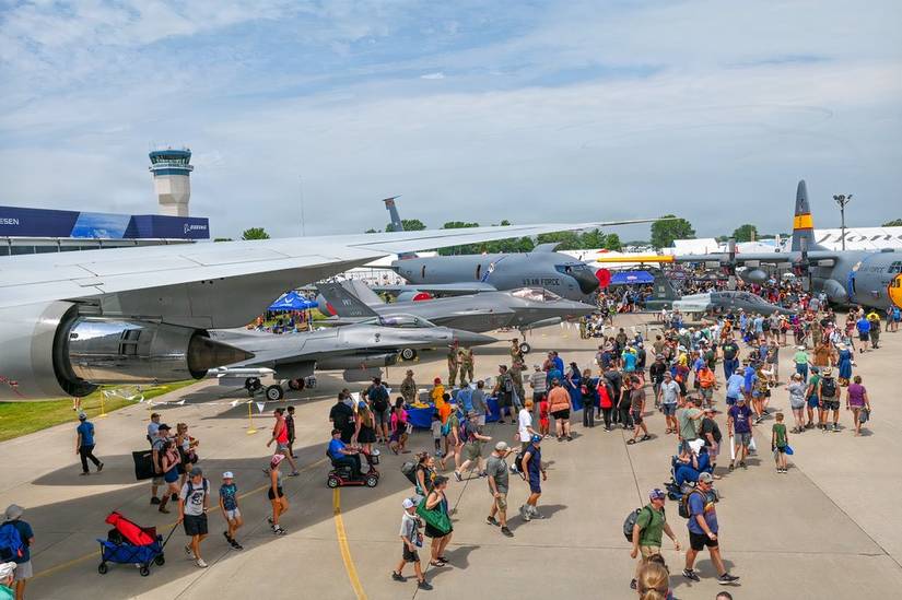 A photo of spectators walking around viewing military aircraft at the EAA AirVenture airshow.