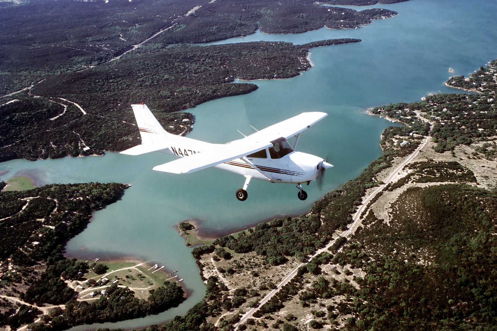 A photo of a Cessna 172 flying over a river with numerous tress on each bank.